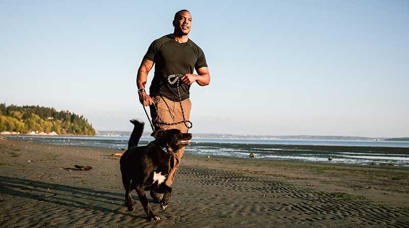 man running with pet dog on beach