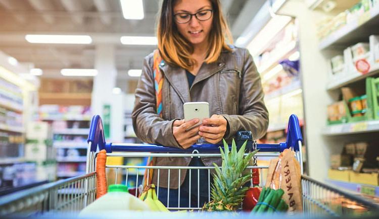 Young women grocery shopping uses her smartphone to view her grocery list. 